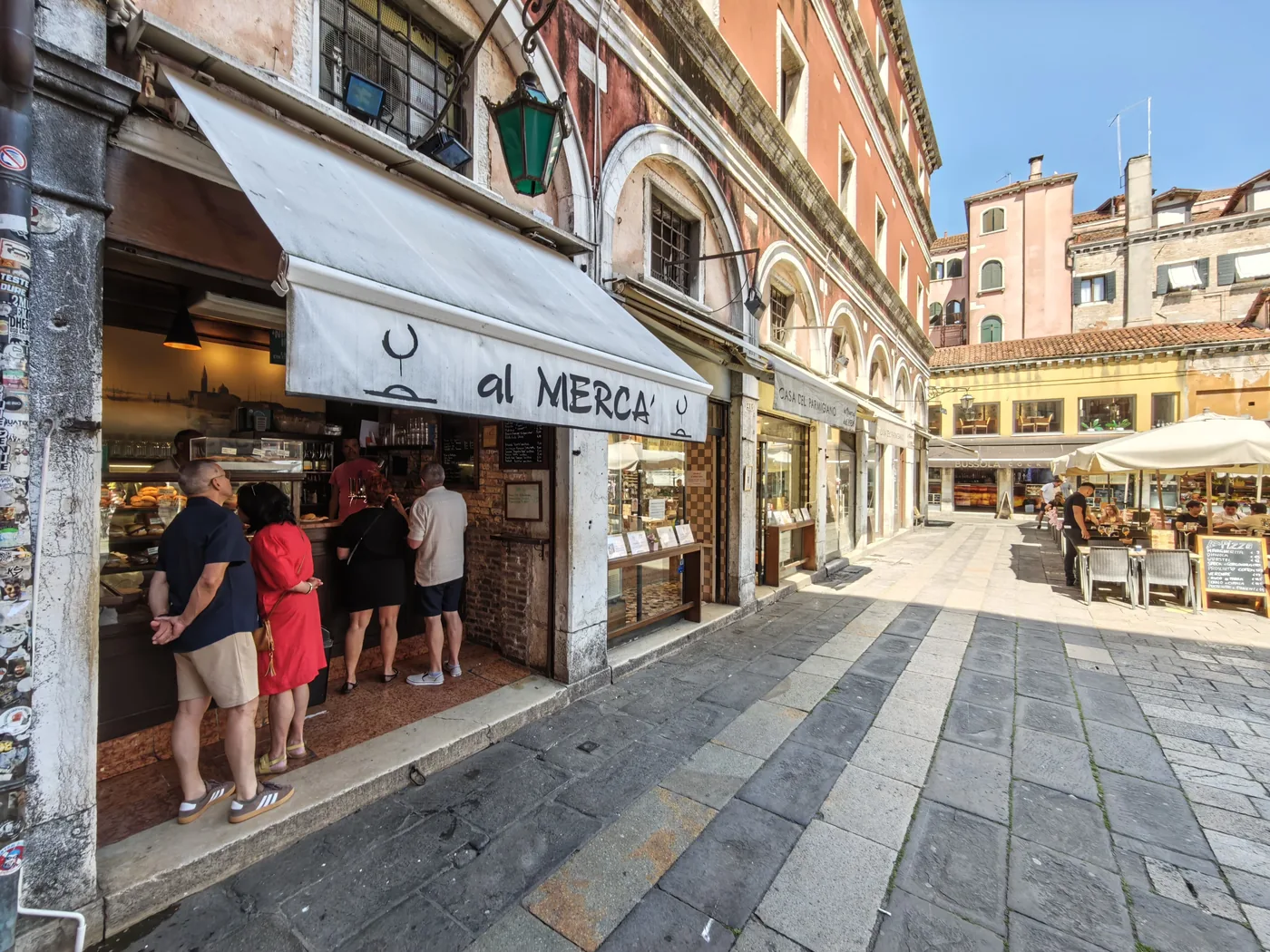 The Al Mercà bacaro on the Rialto square with its white awning and people standing, Venice