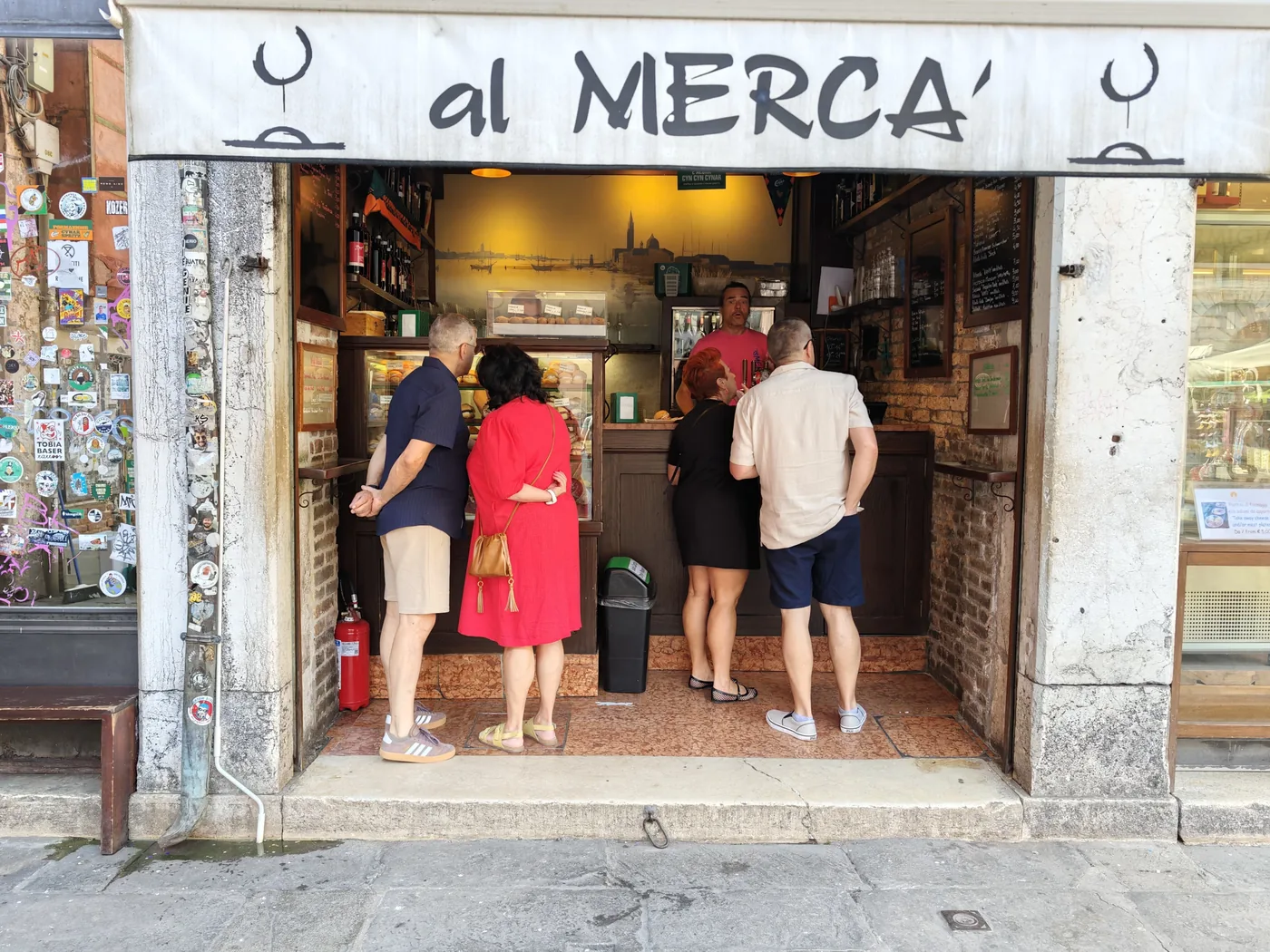 Guests standing at the Al Mercà counter under the white awning, among the lanes of the Rialto market in Venice
